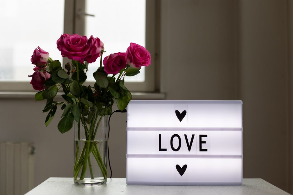 Fresh blossoming flowers in glass vase and bright light box saying Love on table