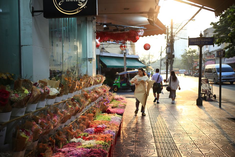 A vibrant urban sidewalk flower shop with people walking by during sunset.