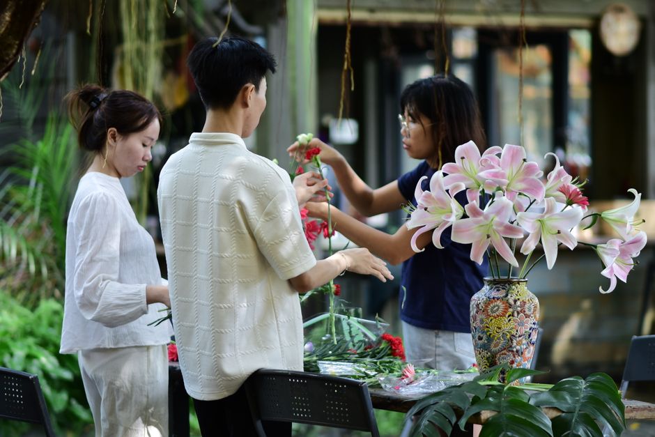 Three people engaged in floral arrangement in a vibrant garden setting, focusing on lilies.