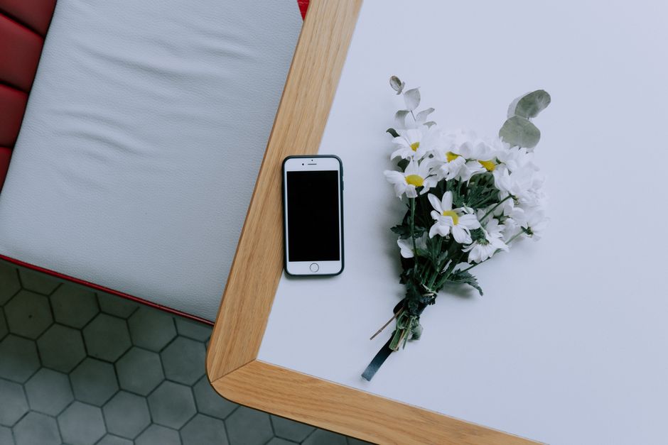 A flat lay showing a smartphone and bouquet on a light wooden table, perfect for technology and lifestyle themes.