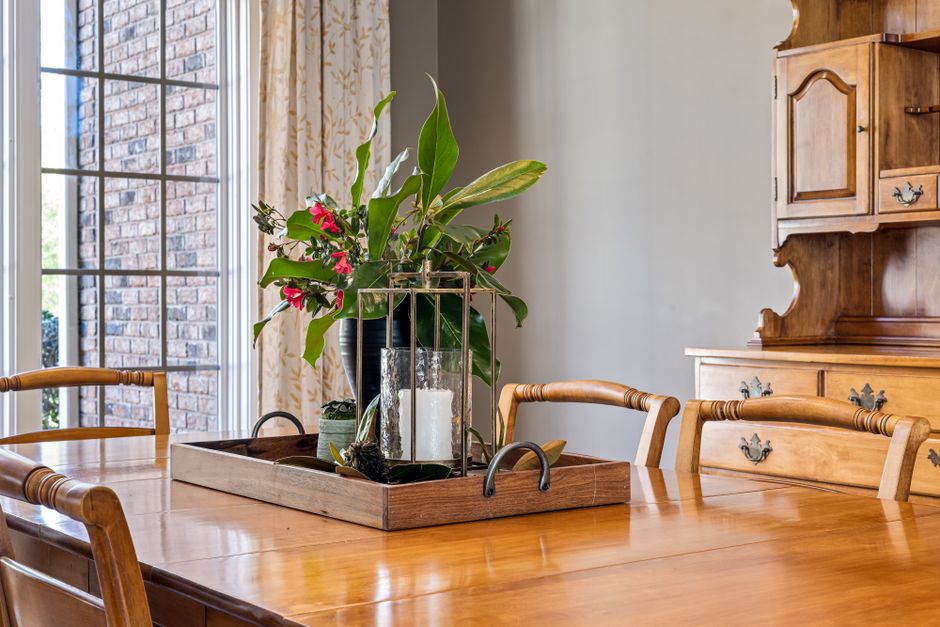 A beautifully arranged flower centerpiece and candle on a wooden dining table in a classic interior setting.
